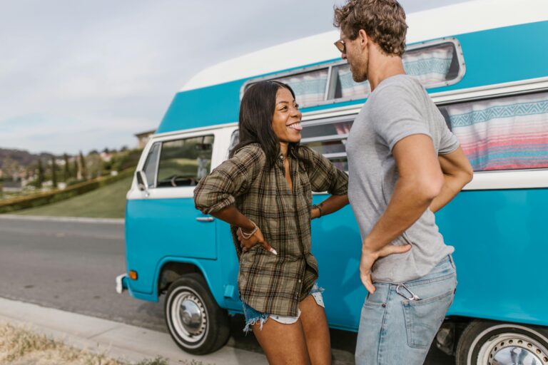 Happy couple dancing and laughing near their campervan on a sunny day, embracing the freedom of van life.
