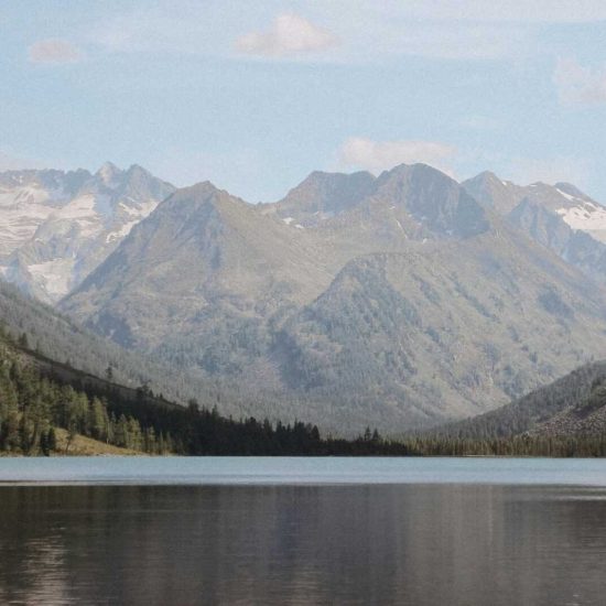 Tranquil lake with majestic Altai mountains and forests under a clear sky.