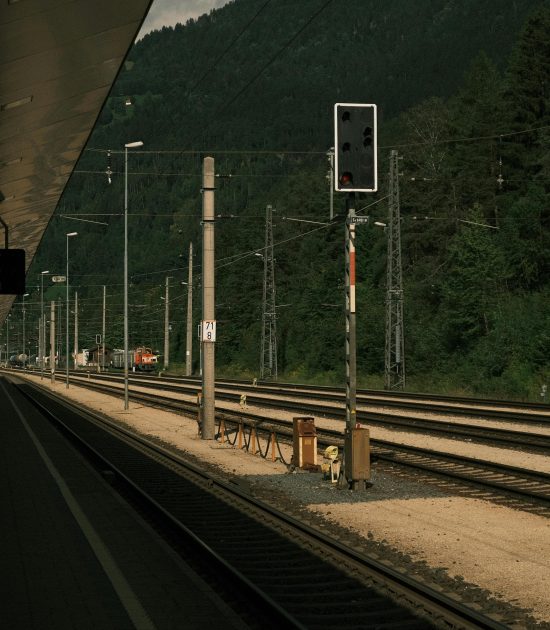 A serene railway station overlooking lush green mountains under a cloudy sky.