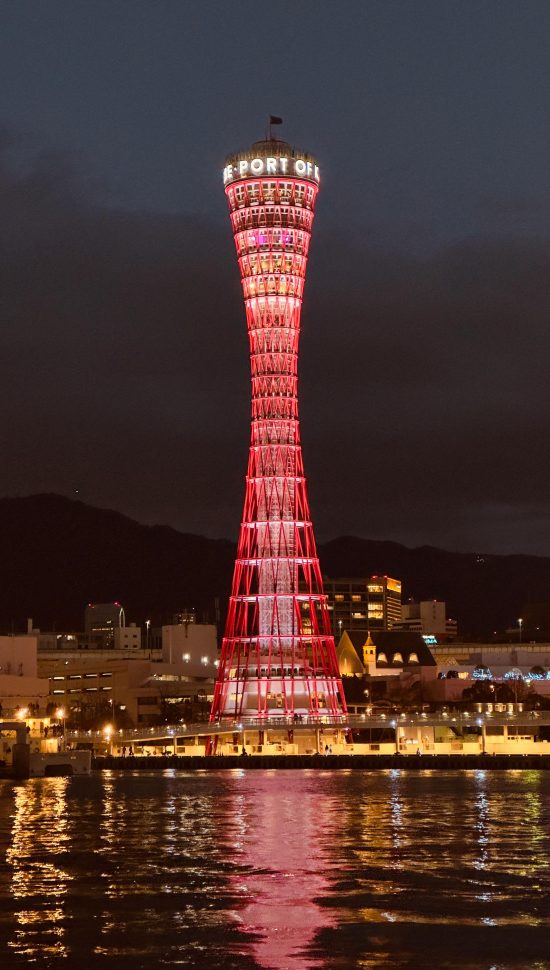 Night view of the illuminated Kobe Port Tower in Japan, reflecting on the water.